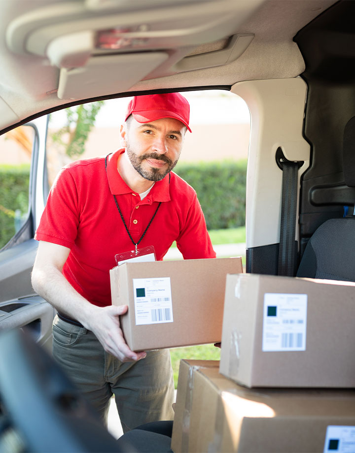 Hombre de entrega con gorra roja y camiseta roja sacando cajas del vehículo de reparto, en un entorno exterior.